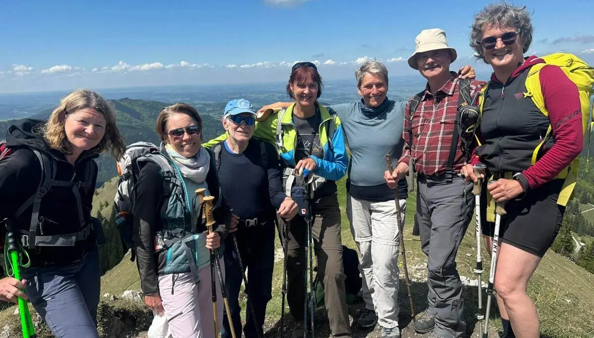 Sieben Wandernde stehen mit Stöcken eng zusammen auf einem Berggipfel; im Hintergrund erstreckt sich eine weite Landschaft unter blauem Himmel. | © DAV Markt Schwaben/Elke Kressirer