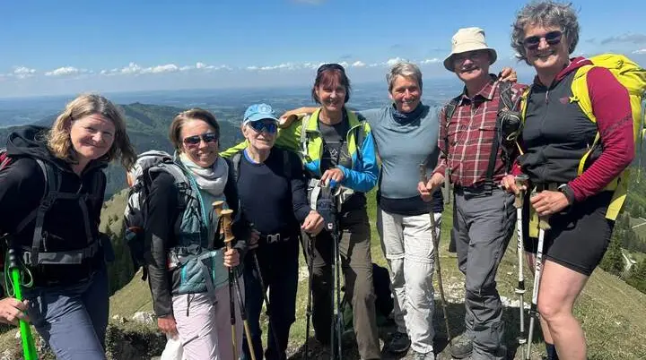 Sieben Wandernde stehen mit Stöcken eng zusammen auf einem Berggipfel; im Hintergrund erstreckt sich eine weite Landschaft unter blauem Himmel. | © DAV Markt Schwaben/Elke Kressirer
