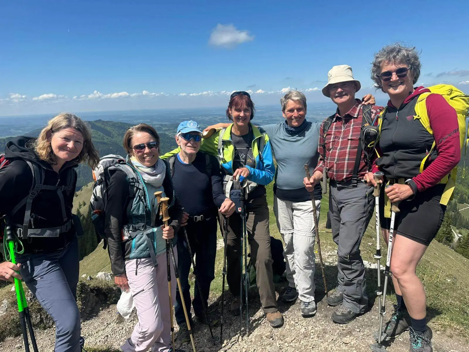Sieben Wandernde stehen mit Stöcken eng zusammen auf einem Berggipfel; im Hintergrund erstreckt sich eine weite Landschaft unter blauem Himmel. | © DAV Markt Schwaben/Elke Kressirer