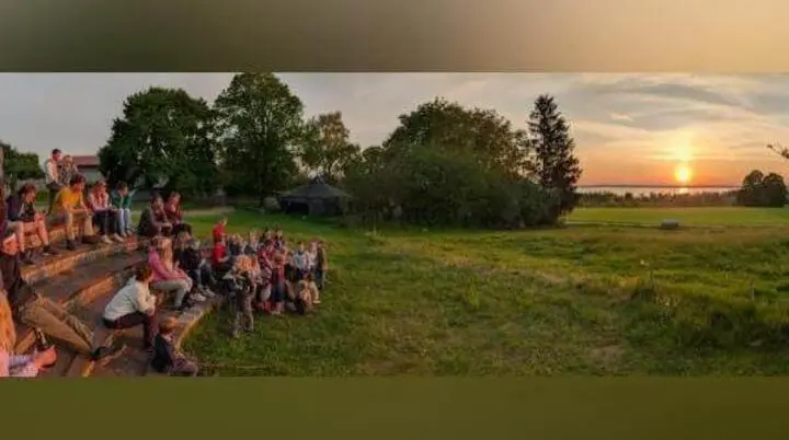 Kinder und Erwachsene sitzen auf Stufen im Freien und blicken auf den Sonnenuntergang über Wiesen und See, ein Tipi steht im Hintergrund. | © DAV Markt Schwaben