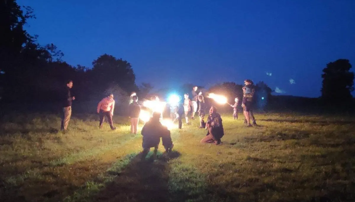 Gruppe von Kindern und Erwachsenen steht nachts auf einer Wiese und hält leuchtende Fackeln; dunkler Himmel und Bäume umgeben die Szene. | © DAV Markt Schwaben
