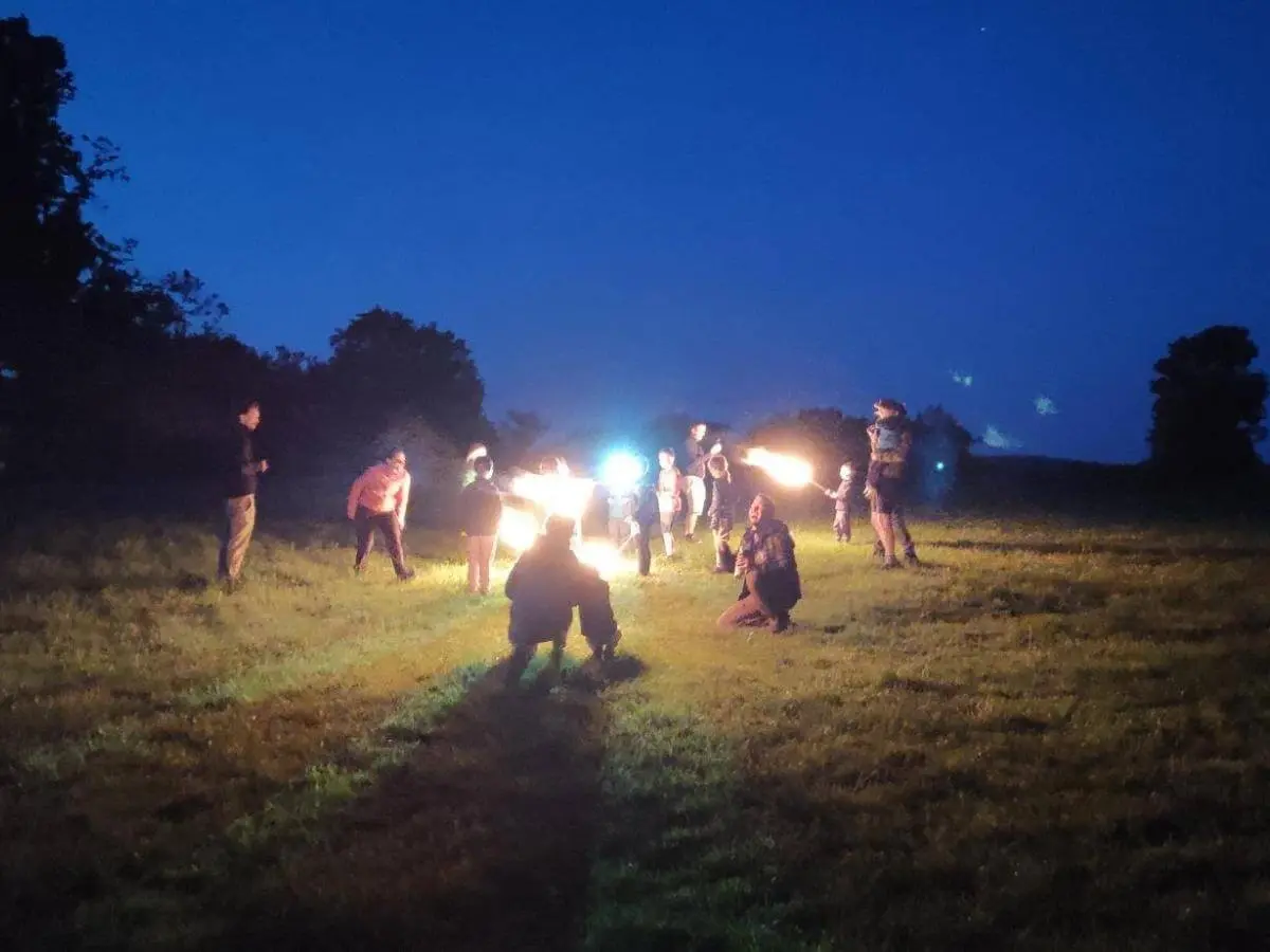 Gruppe von Kindern und Erwachsenen steht nachts auf einer Wiese und hält leuchtende Fackeln; dunkler Himmel und Bäume umgeben die Szene. | © DAV Markt Schwaben