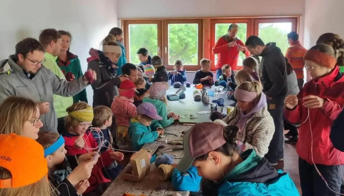 Viele Kinder und Erwachsene sitzen dicht um einen langen Tisch in einer Hütte und knüpfen mit Wolle und Materialien gemeinsam Traumfänger. | © DAV Markt Schwaben