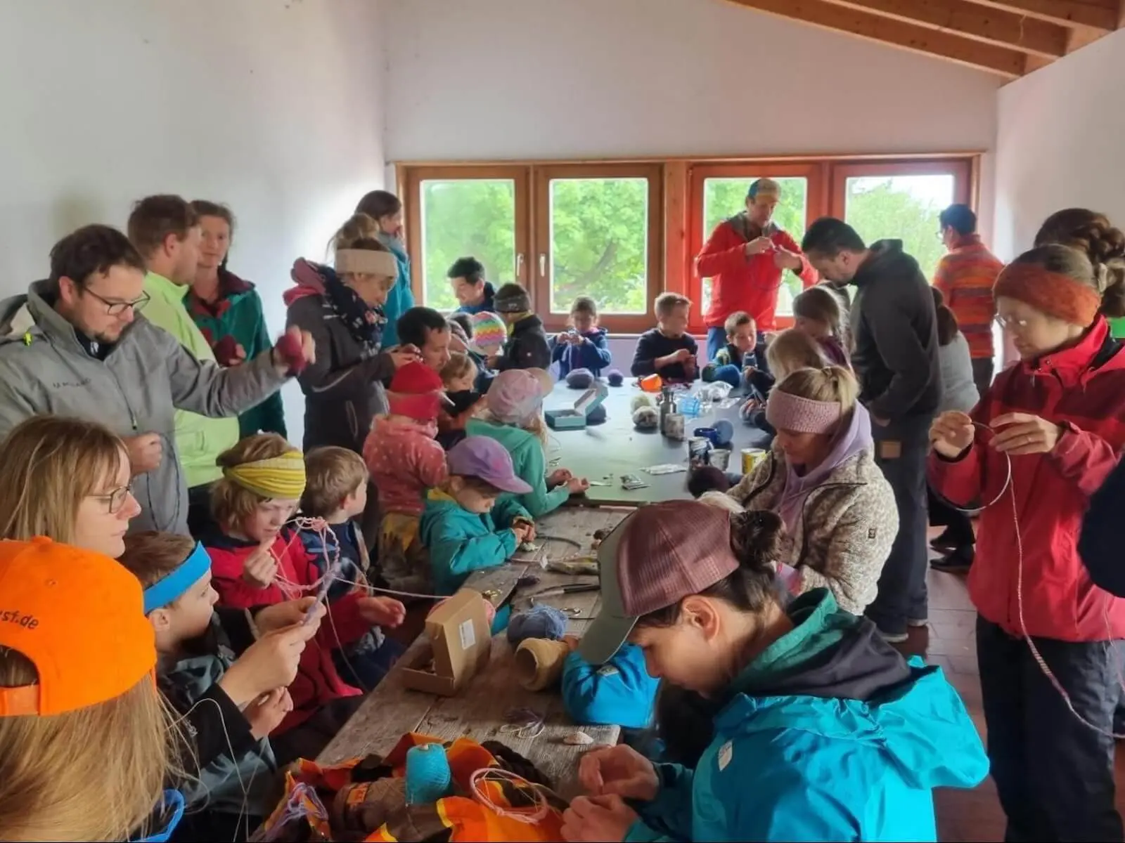 Viele Kinder und Erwachsene sitzen dicht um einen langen Tisch in einer Hütte und knüpfen mit Wolle und Materialien gemeinsam Traumfänger. | © DAV Markt Schwaben
