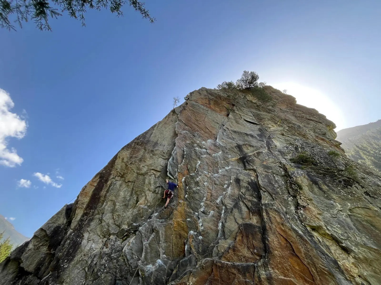 Eine Person klettert gesichert an steiler Felswand im Zillertal, Seil verläuft nach oben; helle Sonne und blauer Himmel im Hintergrund. | © DAV Markt Schwaben