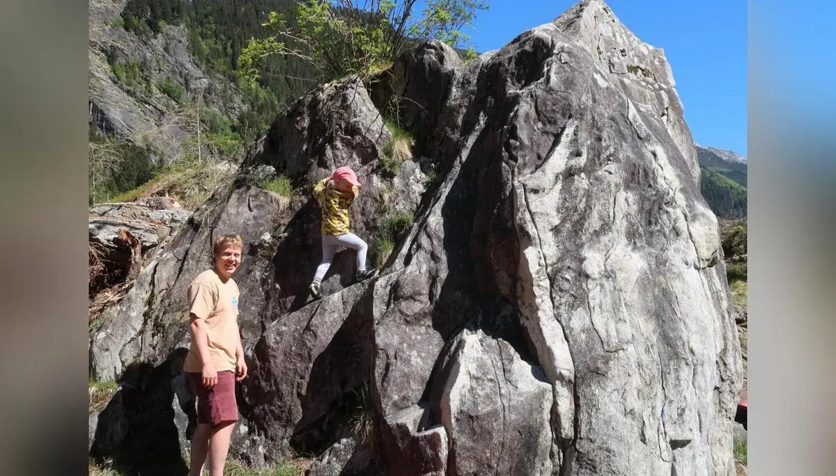 Kind klettert an Felsblock, Person steht daneben auf Crashpads; dahinter Berge und blauer Himmel. | © DAV Markt Schwaben