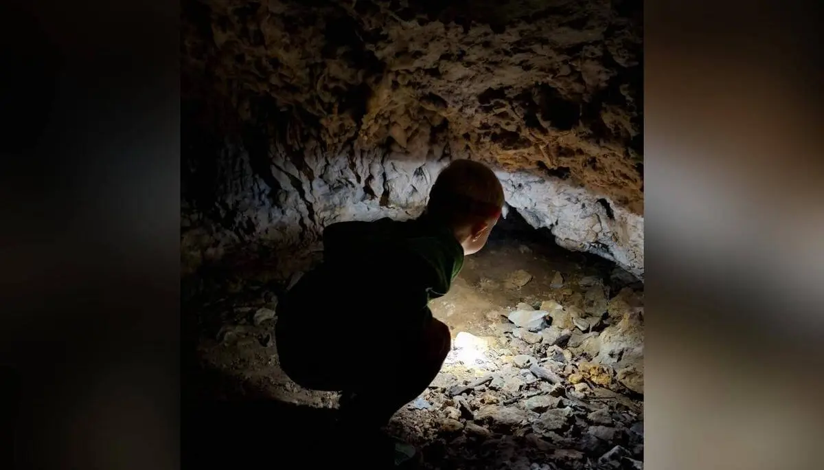Ein Kind hockt in einer kleinen Höhle und leuchtet mit einer Taschenlampe auf den steinigen Boden und die Felswand. | © DAV Markt Schwaben / Lara Wolff