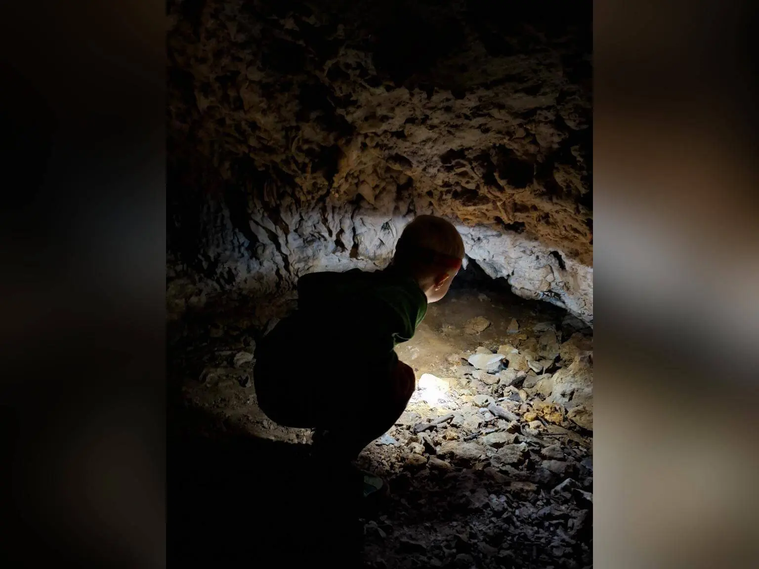 Ein Kind hockt in einer kleinen Höhle und leuchtet mit einer Taschenlampe auf den steinigen Boden und die Felswand. | © DAV Markt Schwaben / Lara Wolff
