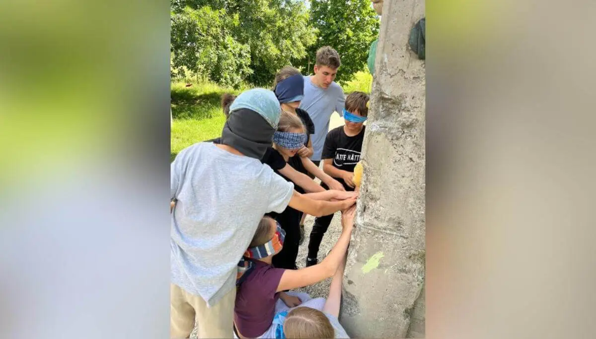 Mehrere Kinder stehen dicht zusammen am Kletterturm und greifen gemeinsam nach einem Objekt, während sie ein Gruppenspiel durchführen. | © DAV Markt Schwaben /  Wiebke Rauschenbach