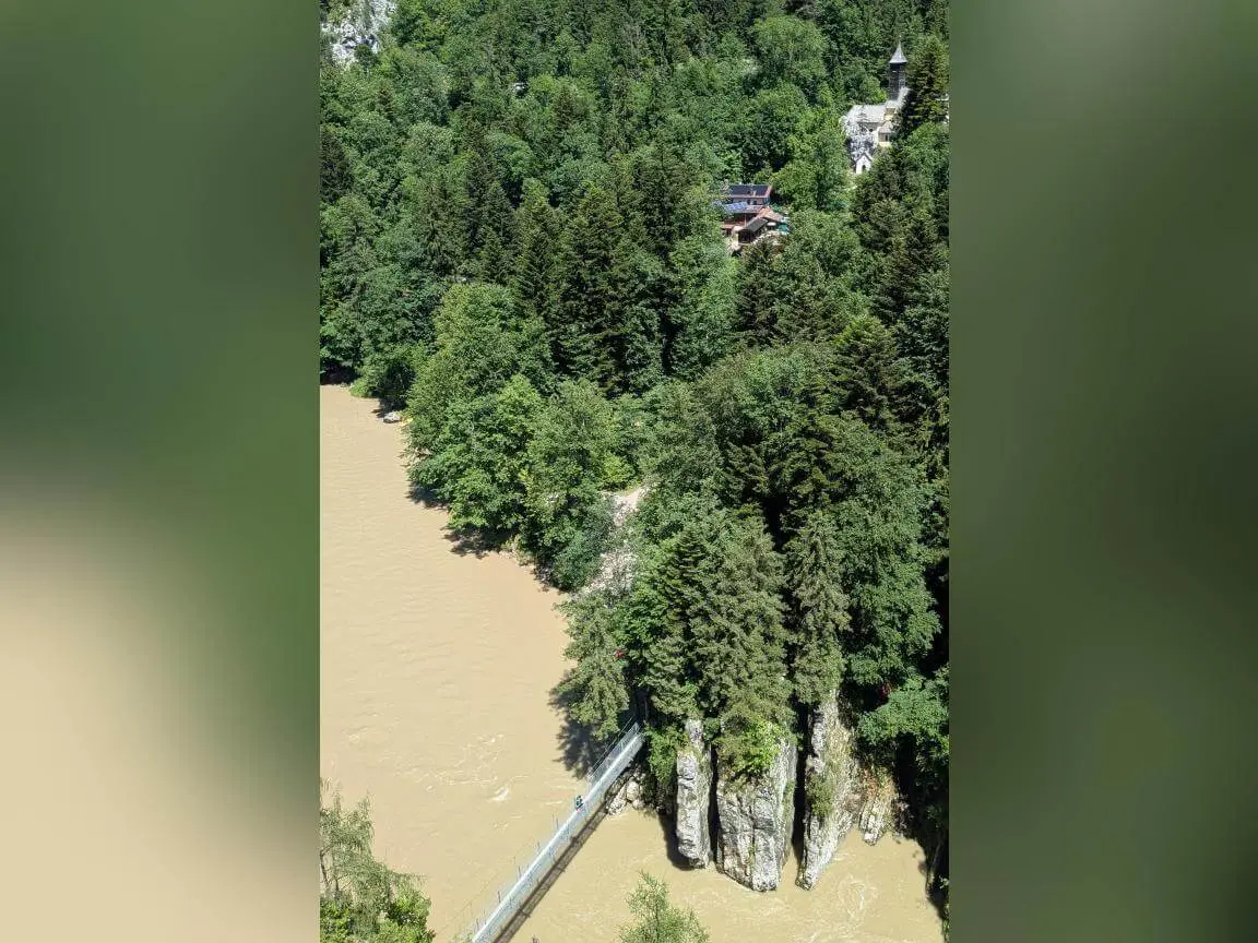 Blick von oben auf eine schmale Hängebrücke über einen braun gefärbten Fluss, umgeben von steilen Felsen und dichtem Wald. | © DAV Markt Schwaben / Silke Titze