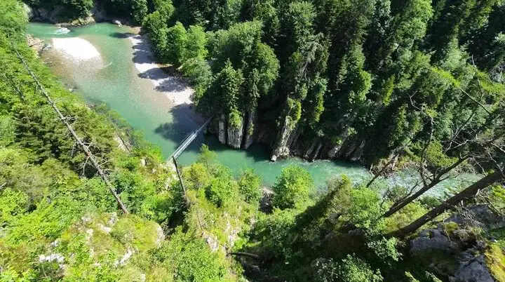 Tiefblick auf die Entenlochklamm mit türkisgrünem Fluss, steilen Felswänden, dichter Bewaldung und einer Hängebrücke. | © DAV Markt Schwaben / Hubert Inhofer
