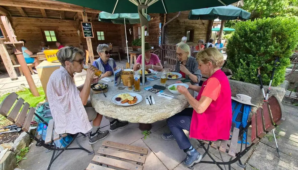 Wandernde sitzen im Biergarten des Gasthauses Klobenstein an einem runden Steintisch und genießen die Mittagspause. | © DAV Markt Schwaben / Hubert Inhofer
