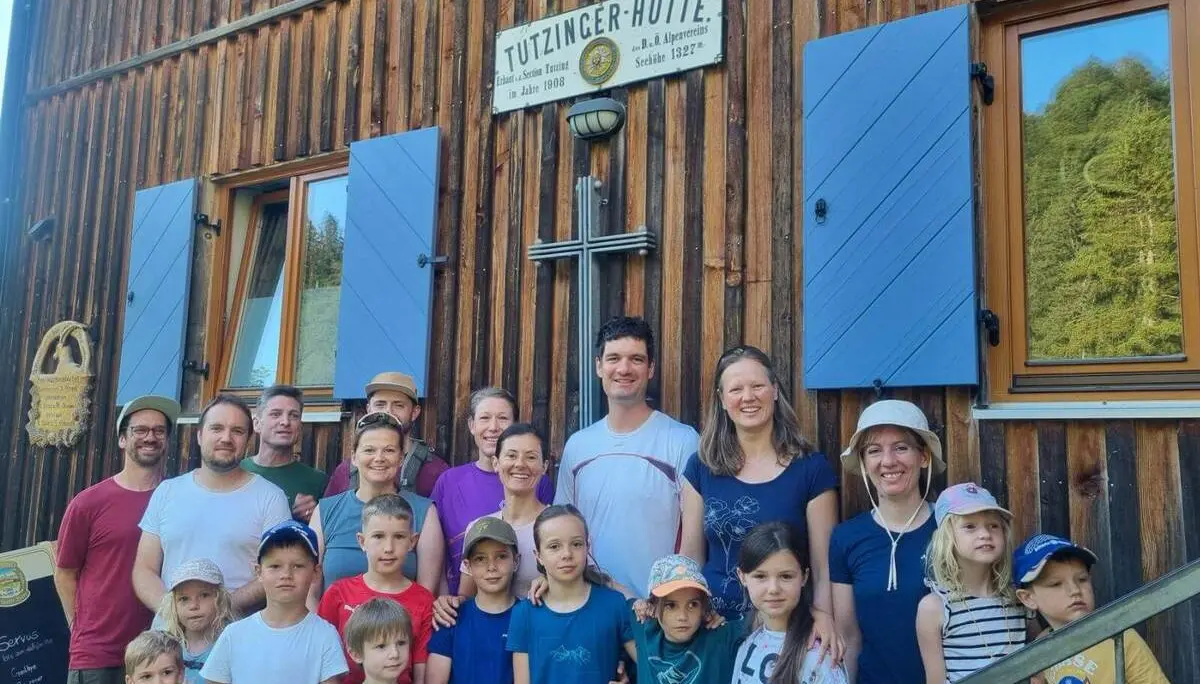 Erwachsene und Kinder stehen vor der Holzfassade der Tutzinger Hütte; über ihnen ist das Hüttenschild mit Höhenangabe sichtbar. | © DAV Markt Schwaben