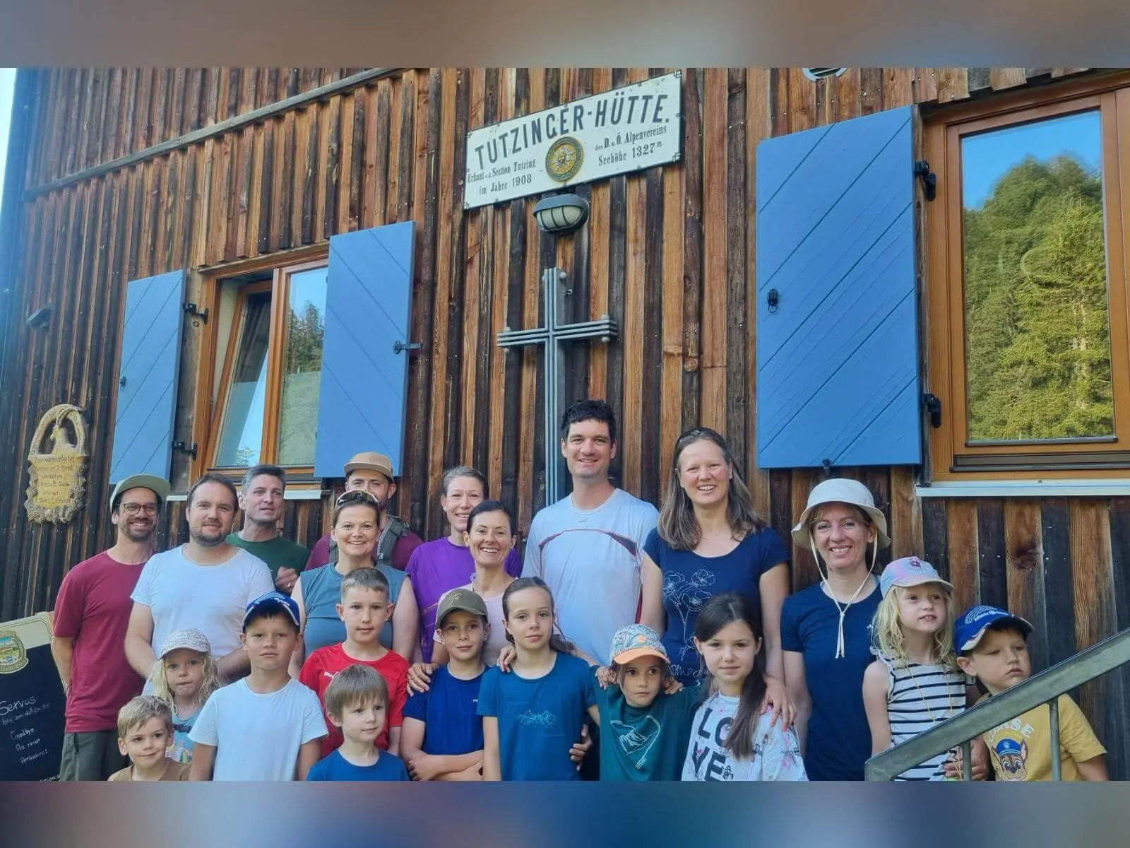 Erwachsene und Kinder stehen vor der Holzfassade der Tutzinger Hütte; über ihnen ist das Hüttenschild mit Höhenangabe sichtbar. | © DAV Markt Schwaben