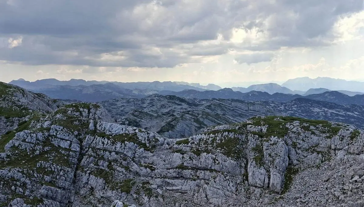 Zerklüftete Kalkfelsen prägen die weite Karstlandschaft des Toten Gebirges. Dunkle Wolken ziehen über den fernen Bergketten auf. | © DAV Markt Schwaben/Alfred Quiel