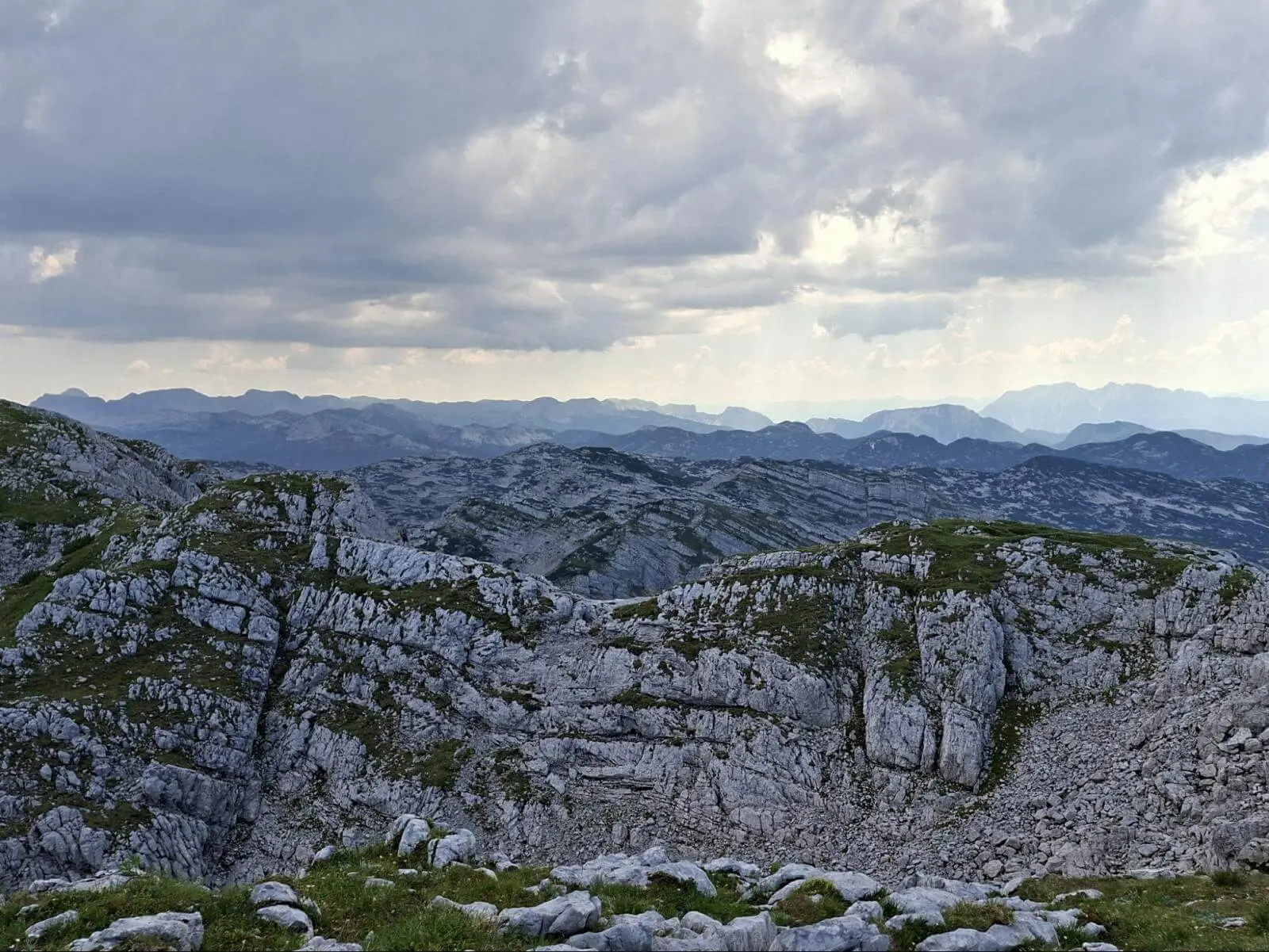Zerklüftete Kalkfelsen prägen die weite Karstlandschaft des Toten Gebirges. Dunkle Wolken ziehen über den fernen Bergketten auf. | © DAV Markt Schwaben/Alfred Quiel