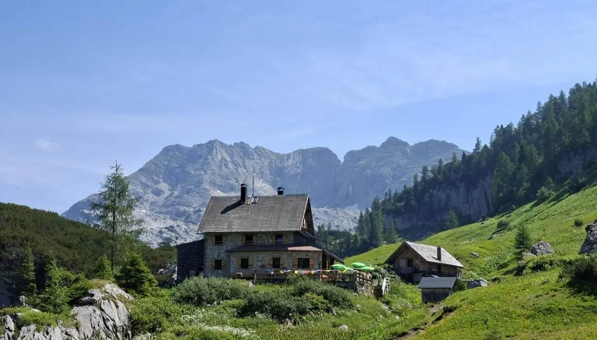 Die Pühringer Hütte steht auf einer grünen Almwiese vor markanten Kalkbergen. Ein schmaler Weg führt durch die Berglandschaft zur Hütte. | © DAV Markt Schwaben/Alfred Quiel