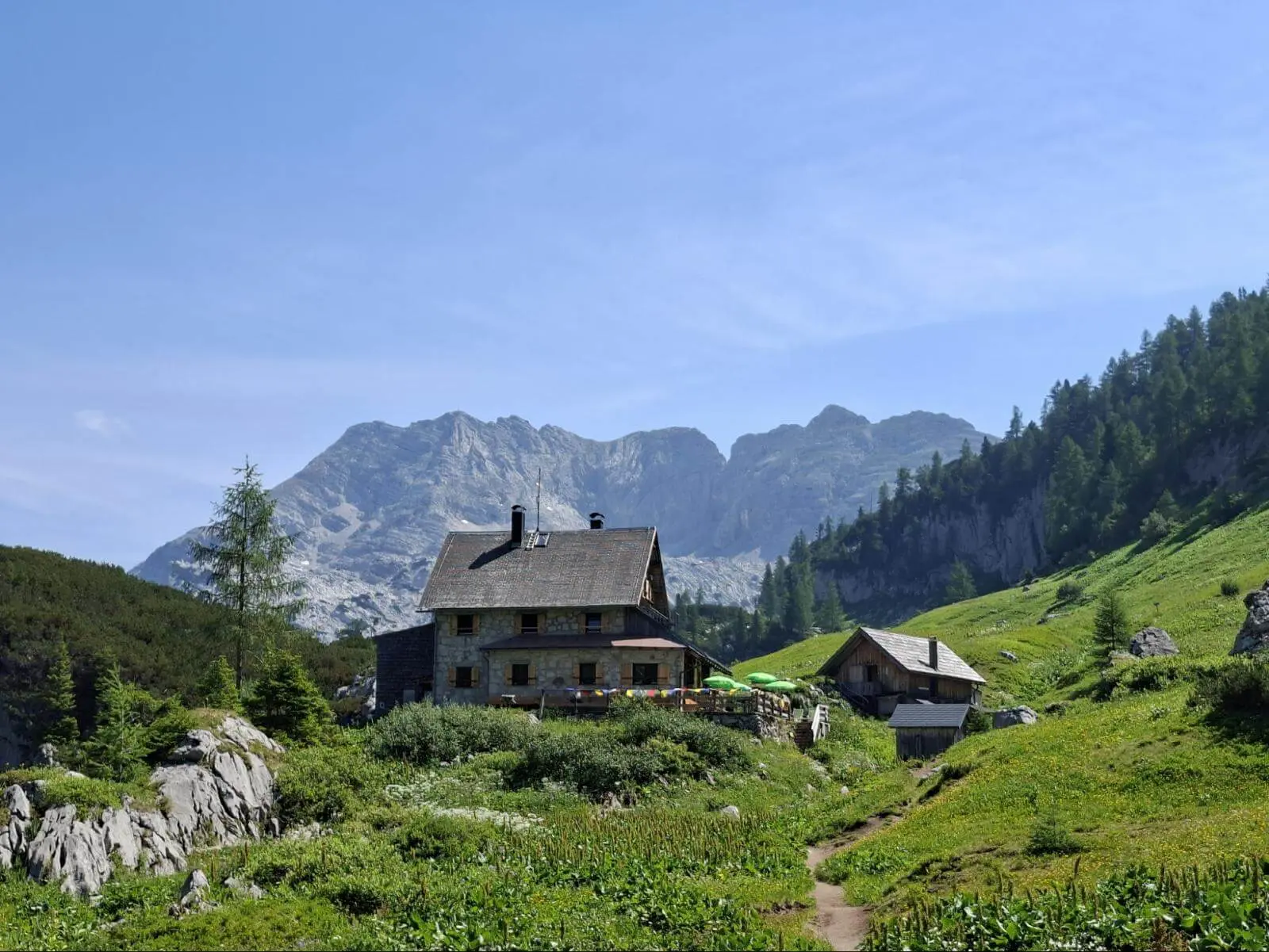 Die Pühringer Hütte steht auf einer grünen Almwiese vor markanten Kalkbergen. Ein schmaler Weg führt durch die Berglandschaft zur Hütte. | © DAV Markt Schwaben/Alfred Quiel
