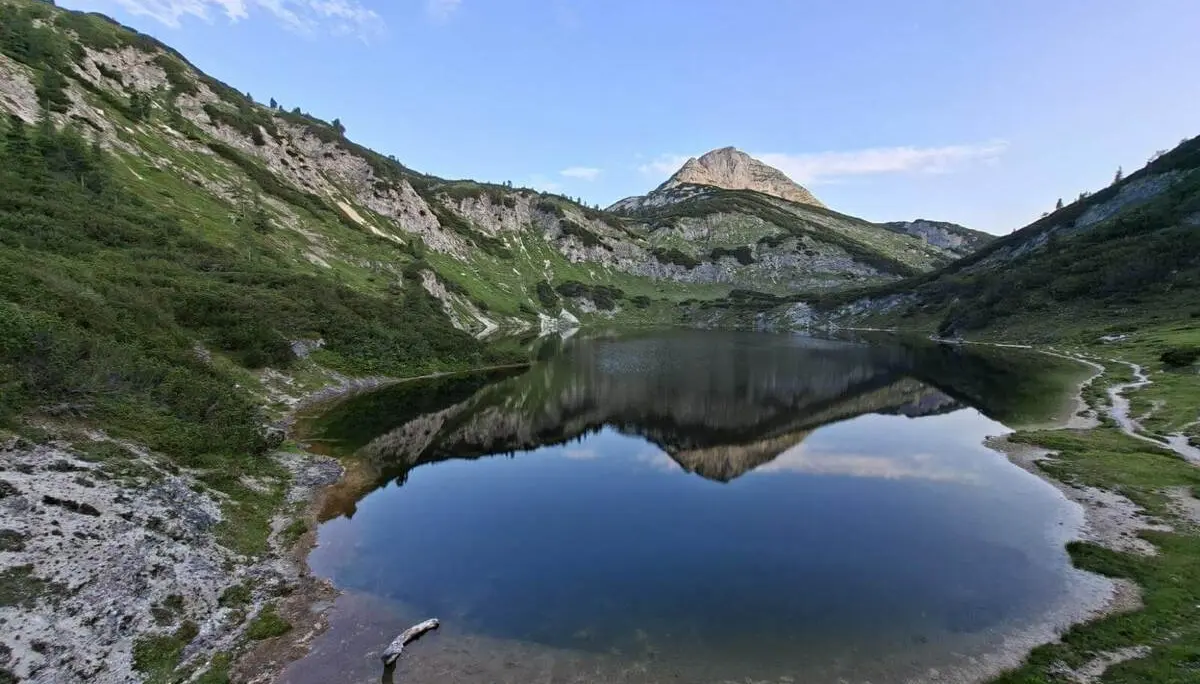 Ein ruhiger Bergsee spiegelt einen markanten Gipfel und die umliegenden Hänge. Uferwege und Karstfelsen säumen das klare Wasser. Show more lines Provide your feedback on BizChat | © DAV Markt Schwaben/Alfred Quiel