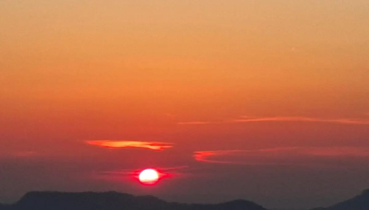Die tiefstehende Sonne leuchtet rot am Horizont über dunklen Bergsilhouetten. Orangefarbene Wolken prägen den Abendhimmel. | © DAV Markt Schwaben/Alfred Quiel