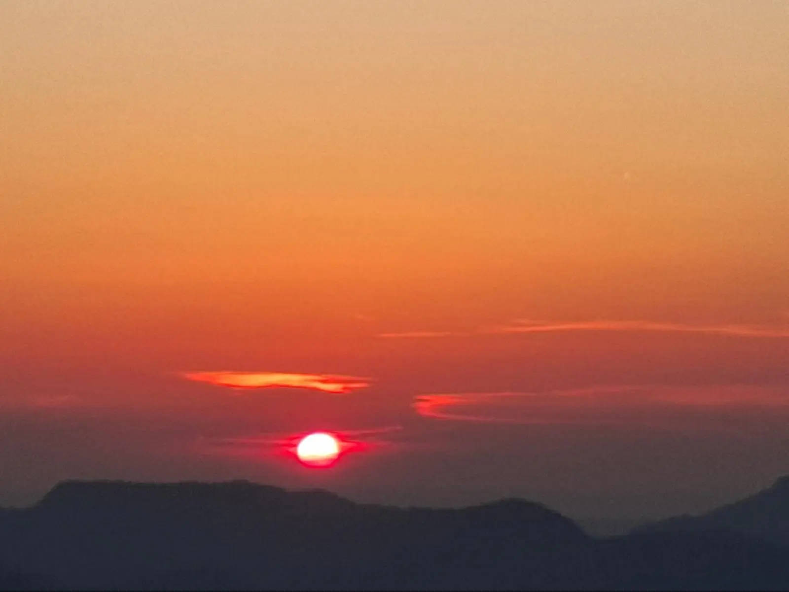 Die tiefstehende Sonne leuchtet rot am Horizont über dunklen Bergsilhouetten. Orangefarbene Wolken prägen den Abendhimmel. | © DAV Markt Schwaben/Alfred Quiel