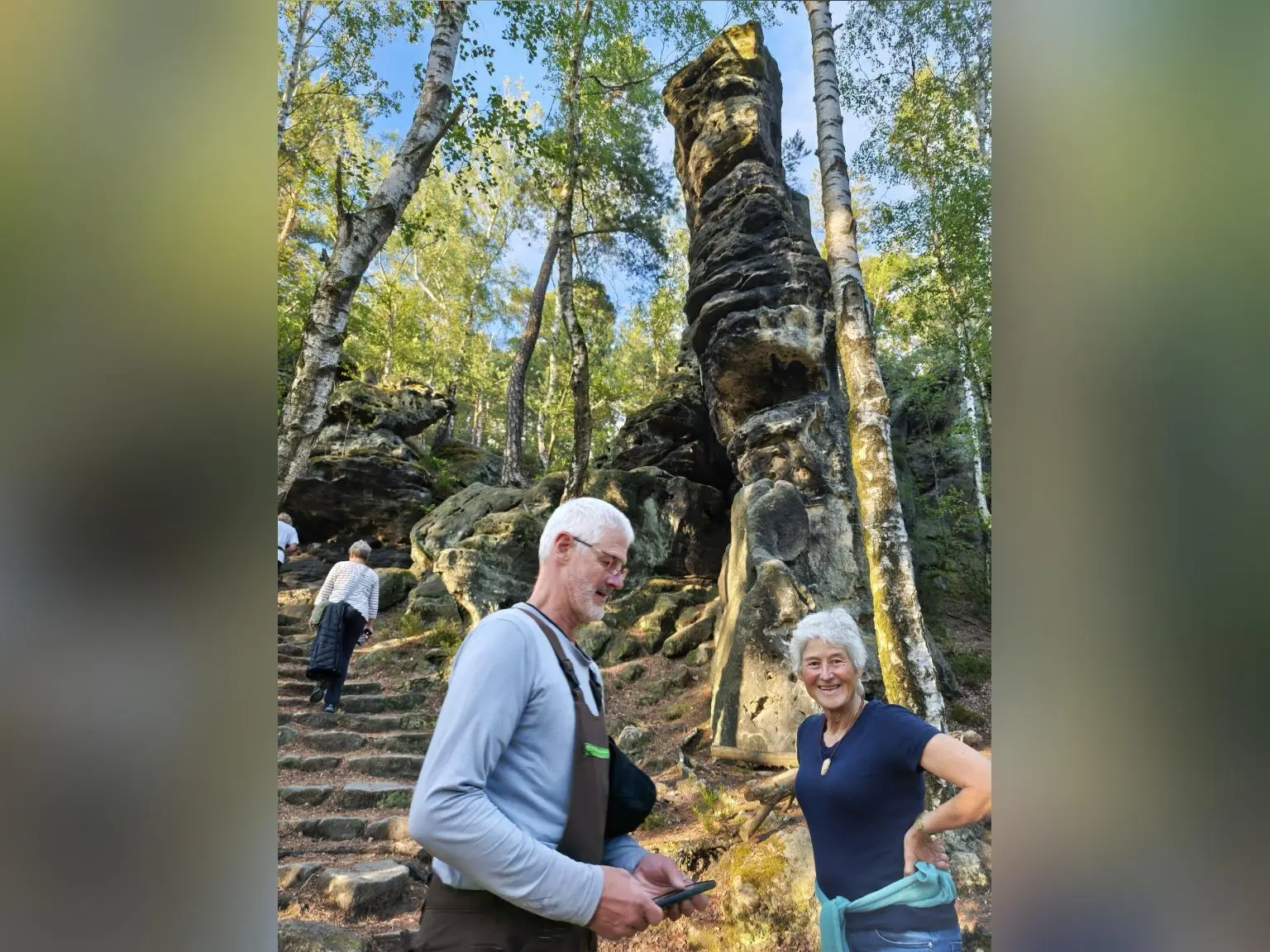 Zwei Wandernde stehen vor einer markanten Sandsteinfelsnadel im Wald; eine Steintreppe führt zwischen Birken zum Felsen. | © DAV Markt Schwaben/Erwin&Ursula Matzinger