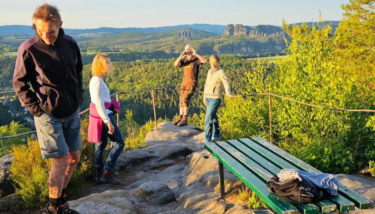 Wandergruppe auf einem Felsplateau mit Bank und Geländer. Im Hintergrund erstrecken sich bewaldete Hügel und markante Sandsteinfelsen. | © DAV Markt Schwaben/Lutz Gründel