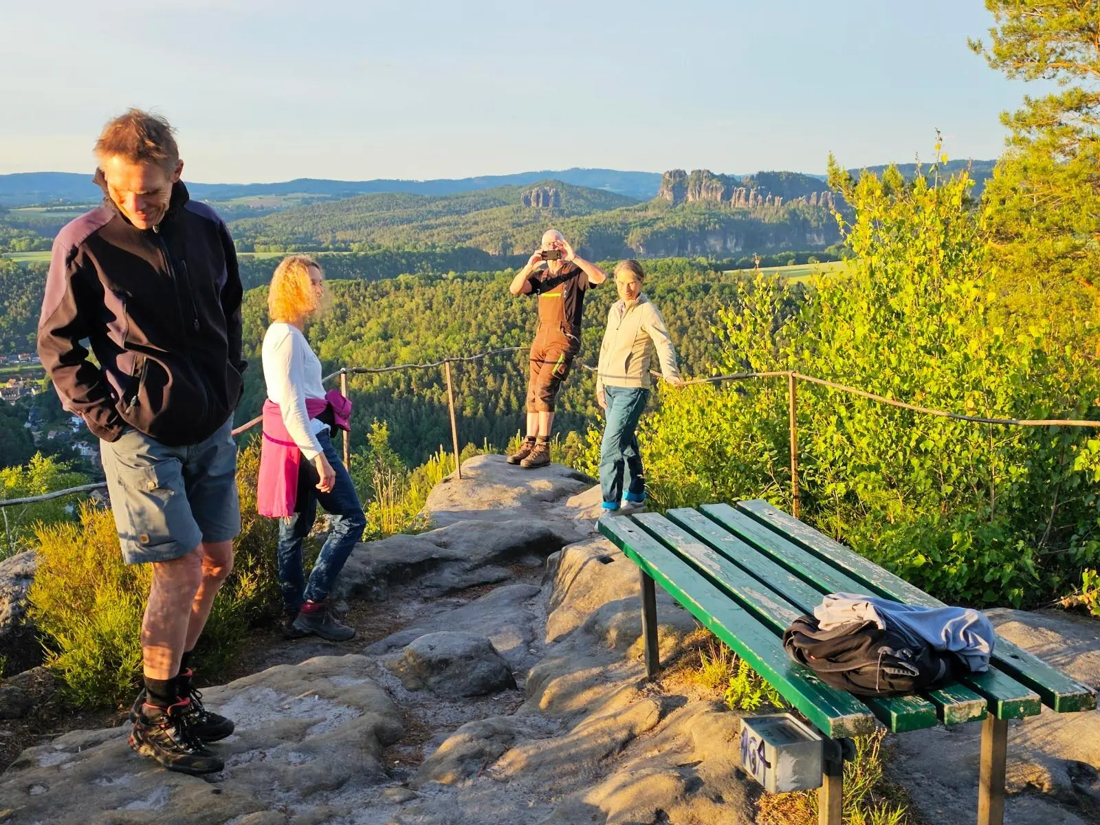 Wandergruppe auf einem Felsplateau mit Bank und Geländer. Im Hintergrund erstrecken sich bewaldete Hügel und markante Sandsteinfelsen. | © DAV Markt Schwaben/Lutz Gründel