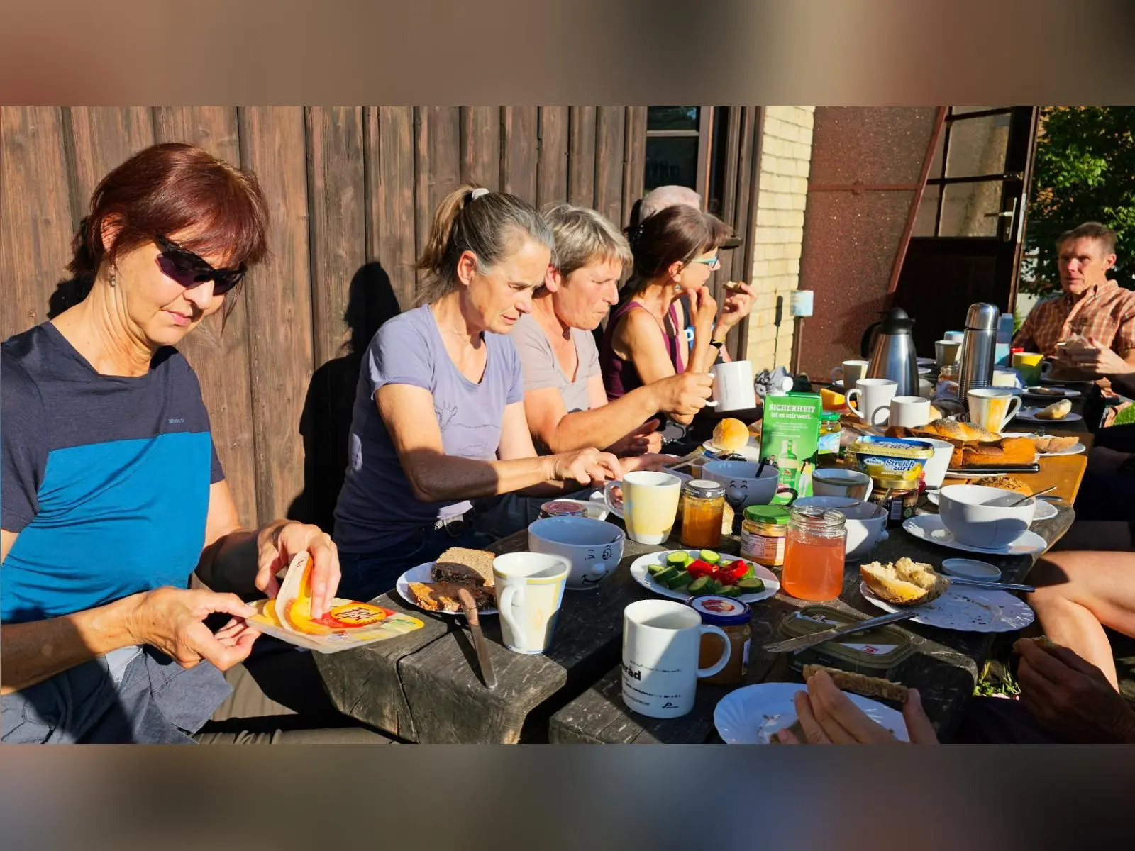 Mehrere Tourenteilnehmende sitzen an einem gedeckten Tisch im Freien. Auf dem Tisch stehen Brot, Aufstriche, Gemüse und Heißgetränke im Morgenlicht. | © DAV Markt Schwaben/Lutz Gründel
