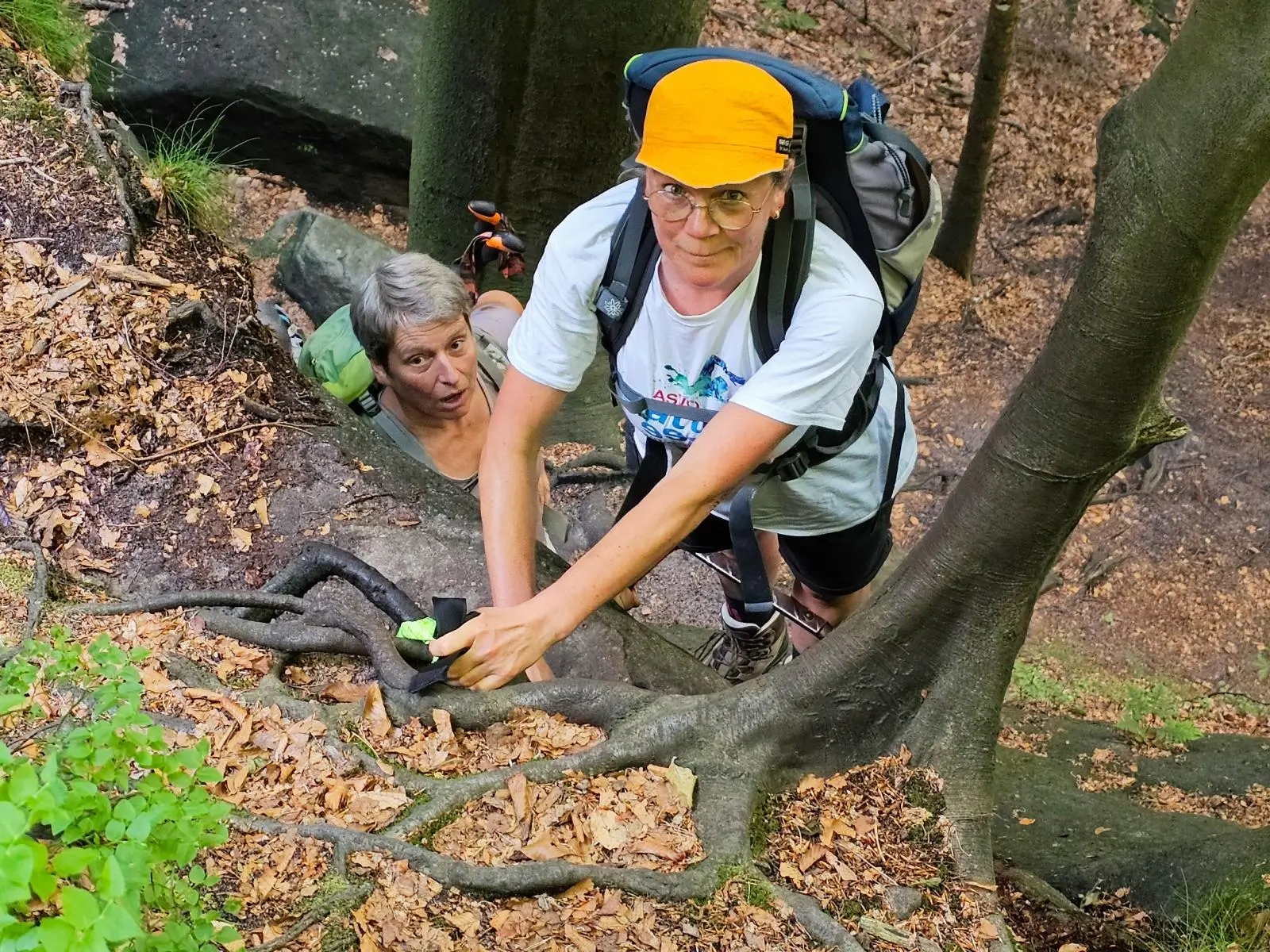 Zwei Wandernde steigen durch eine schmale Felsspalte bergauf. Freiliegende Baumwurzeln dienen dabei als natürliche Tritthilfe. | © DAV Markt Schwaben/Lutz Gründel