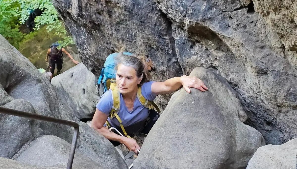 Eine Person steigt mit Rucksack durch eine enge Felsschlucht und hält sich an einer Eisenstufe fest; weitere Wandernde folgen darunter. | © DAV Markt Schwaben/Lutz Gründel