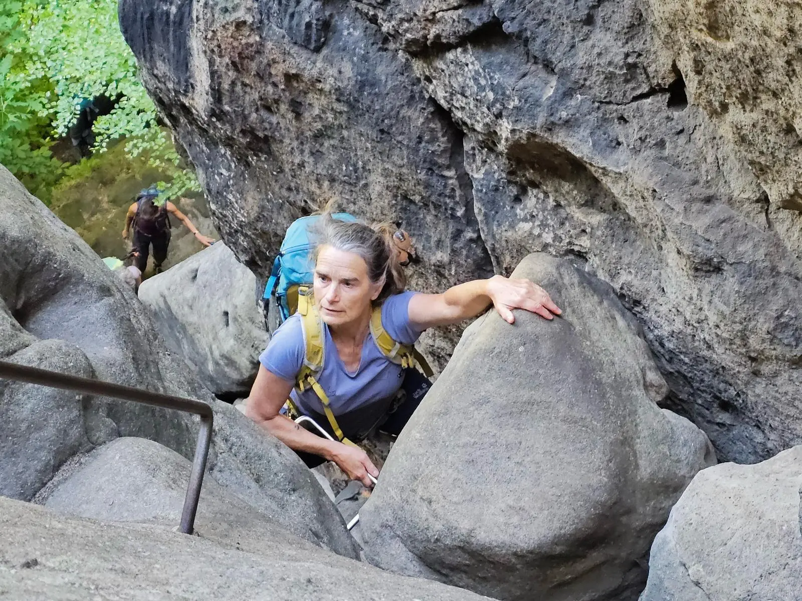 Eine Person steigt mit Rucksack durch eine enge Felsschlucht und hält sich an einer Eisenstufe fest; weitere Wandernde folgen darunter. | © DAV Markt Schwaben/Lutz Gründel
