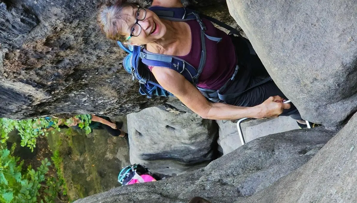Eine Wandernde steigt auf Eisenstufen durch eine enge Felsspalte zwischen großen Sandsteinblöcken; weitere Personen folgen darunter. | © DAV Markt Schwaben/Lutz Gründel