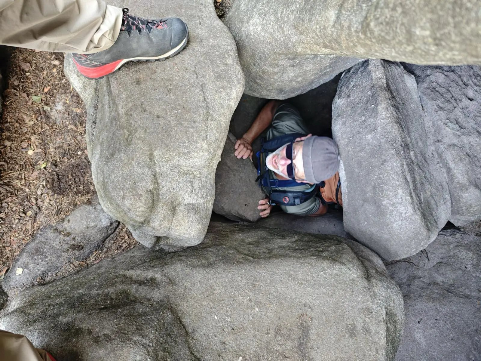 Eine Person zwängt sich mit Rucksack durch eine schmale Öffnung zwischen großen Sandsteinblöcken; Wanderschuhe sind am oberen Rand sichtbar. | © DAV Markt Schwaben/Erwin&Ursula Matzinger