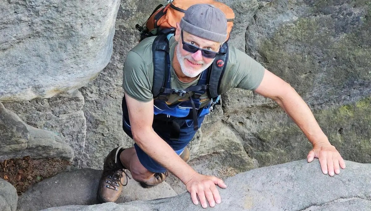 Eine Person mit Rucksack klettert durch eine enge Sandsteinpassage und stützt sich mit beiden Händen auf den Felsrand. | © DAV Markt Schwaben/Lutz Gründel