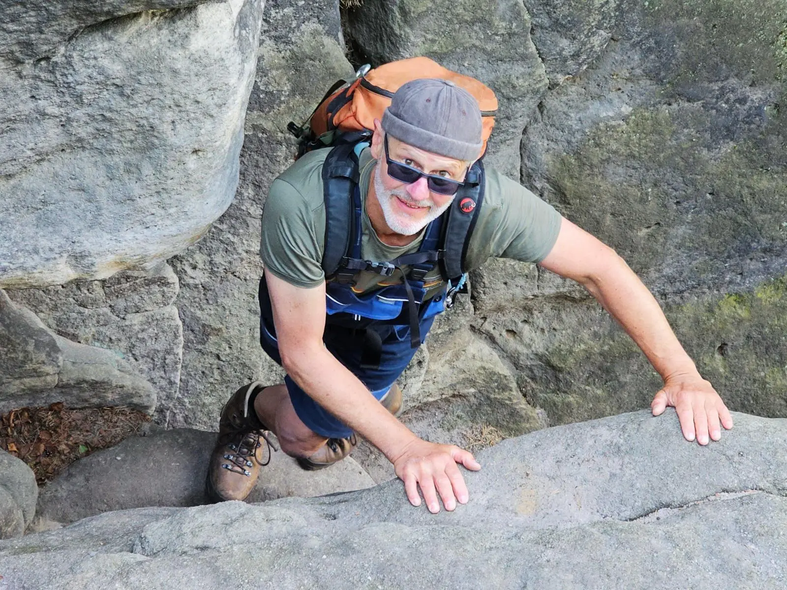 Eine Person mit Rucksack klettert durch eine enge Sandsteinpassage und stützt sich mit beiden Händen auf den Felsrand. | © DAV Markt Schwaben/Lutz Gründel