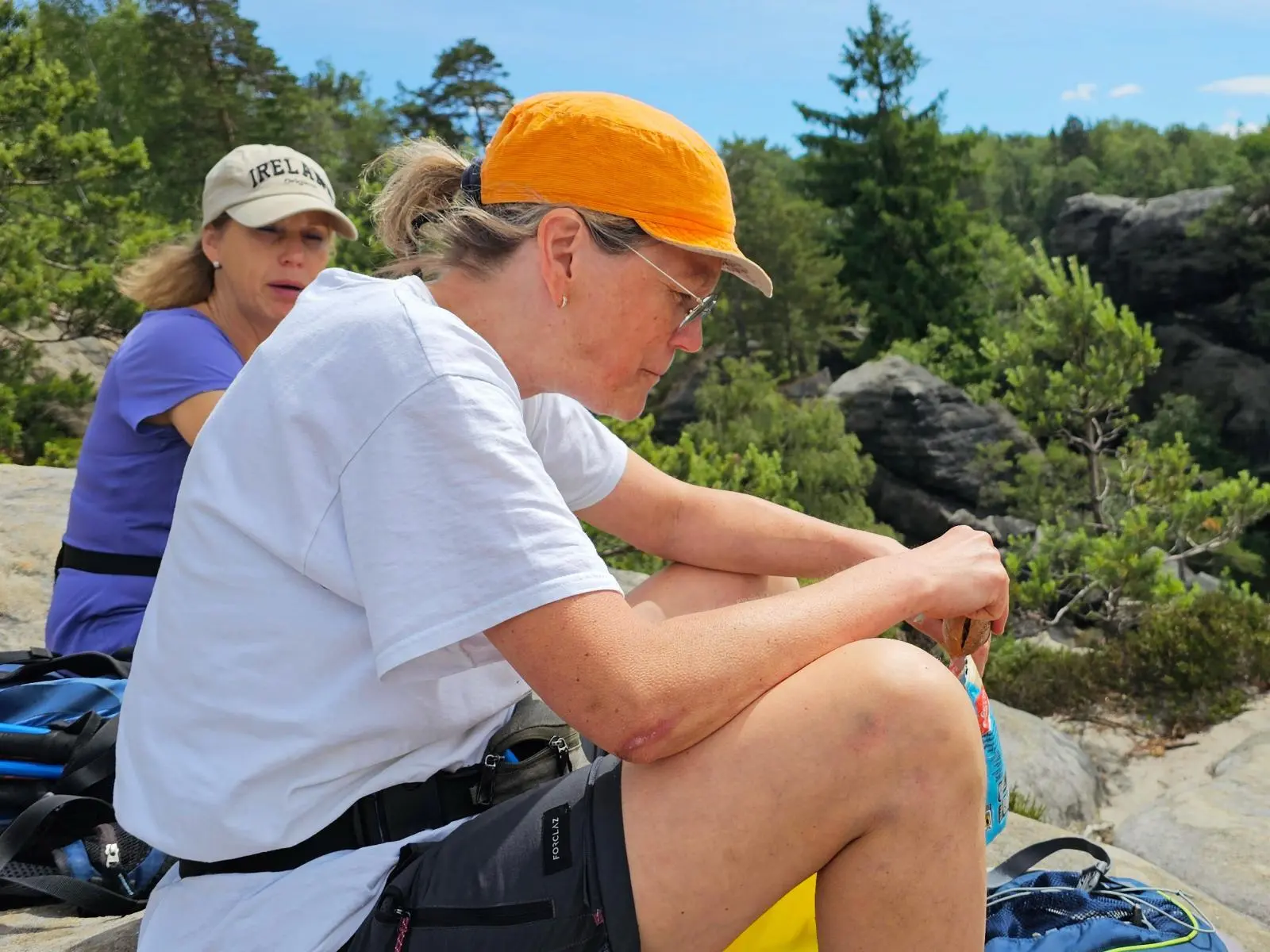Zwei Wandernde sitzen während einer Pause auf einem Sandsteinfelsen. Im Hintergrund liegen Kiefern, Felsen und bewaldete Hänge der Sächsischen Schweiz. | © DAV Markt Schwaben/Lutz Gründel