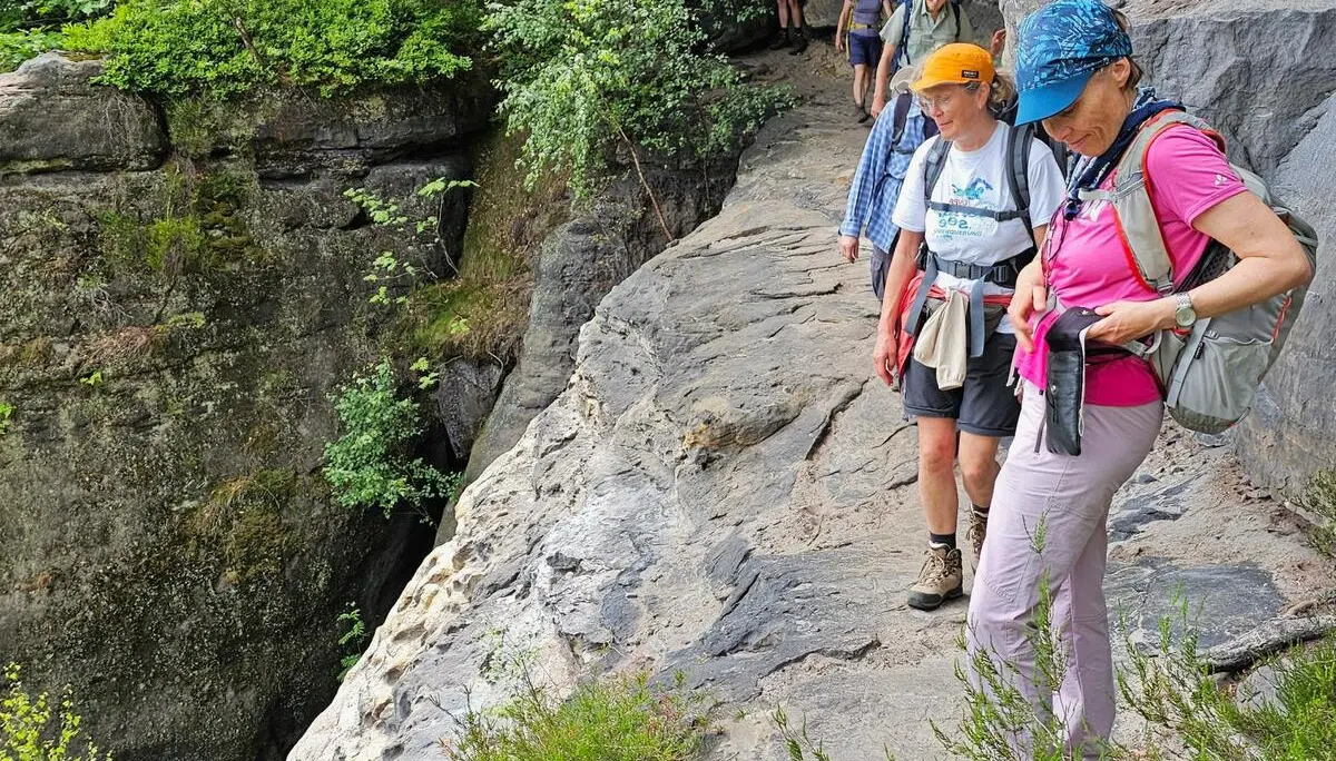 Mehrere Wandernde gehen auf einem schmalen Felsband entlang einer Sandsteinwand. Daneben fällt das Gelände steil in eine bewaldete Schlucht ab. | © DAV Markt Schwaben/Lutz Gründel