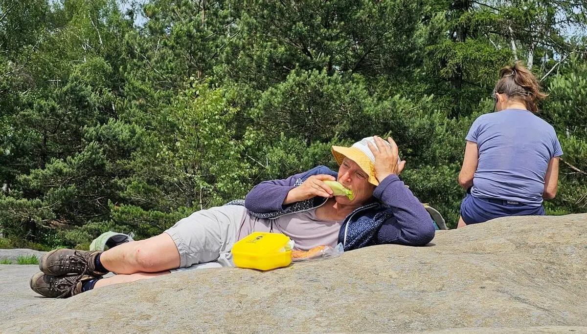 Eine Person liegt während einer Wanderpause auf einer Felsplatte und isst. Daneben sitzt eine weitere Person vor dichtem Kiefernwald. | © DAV Markt Schwaben/Lutz Gründel