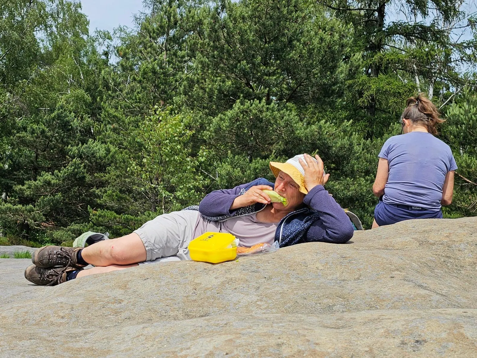 Eine Person liegt während einer Wanderpause auf einer Felsplatte und isst. Daneben sitzt eine weitere Person vor dichtem Kiefernwald. | © DAV Markt Schwaben/Lutz Gründel