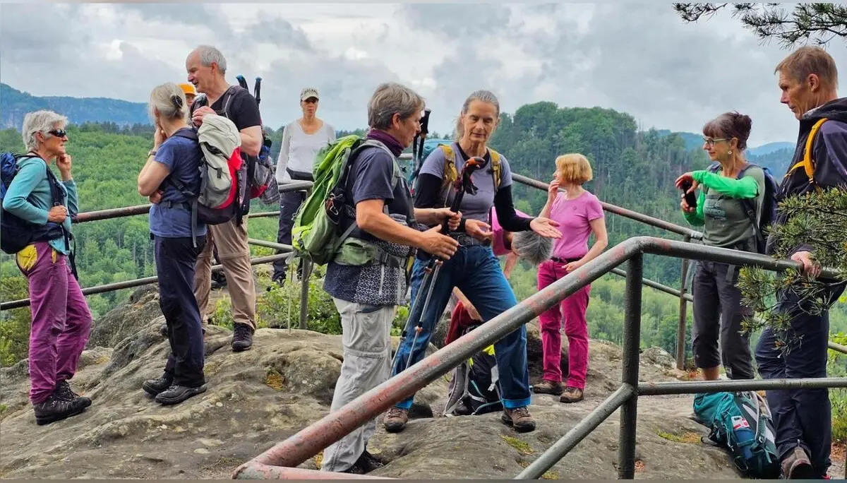 Eine Wandergruppe steht auf einem felsigen Aussichtspunkt mit Geländer. Im Hintergrund erstrecken sich bewaldete Hügel und Sandsteinfelsen der Sächsischen Schweiz. | © DAV Markt Schwaben/Lutz Gründel