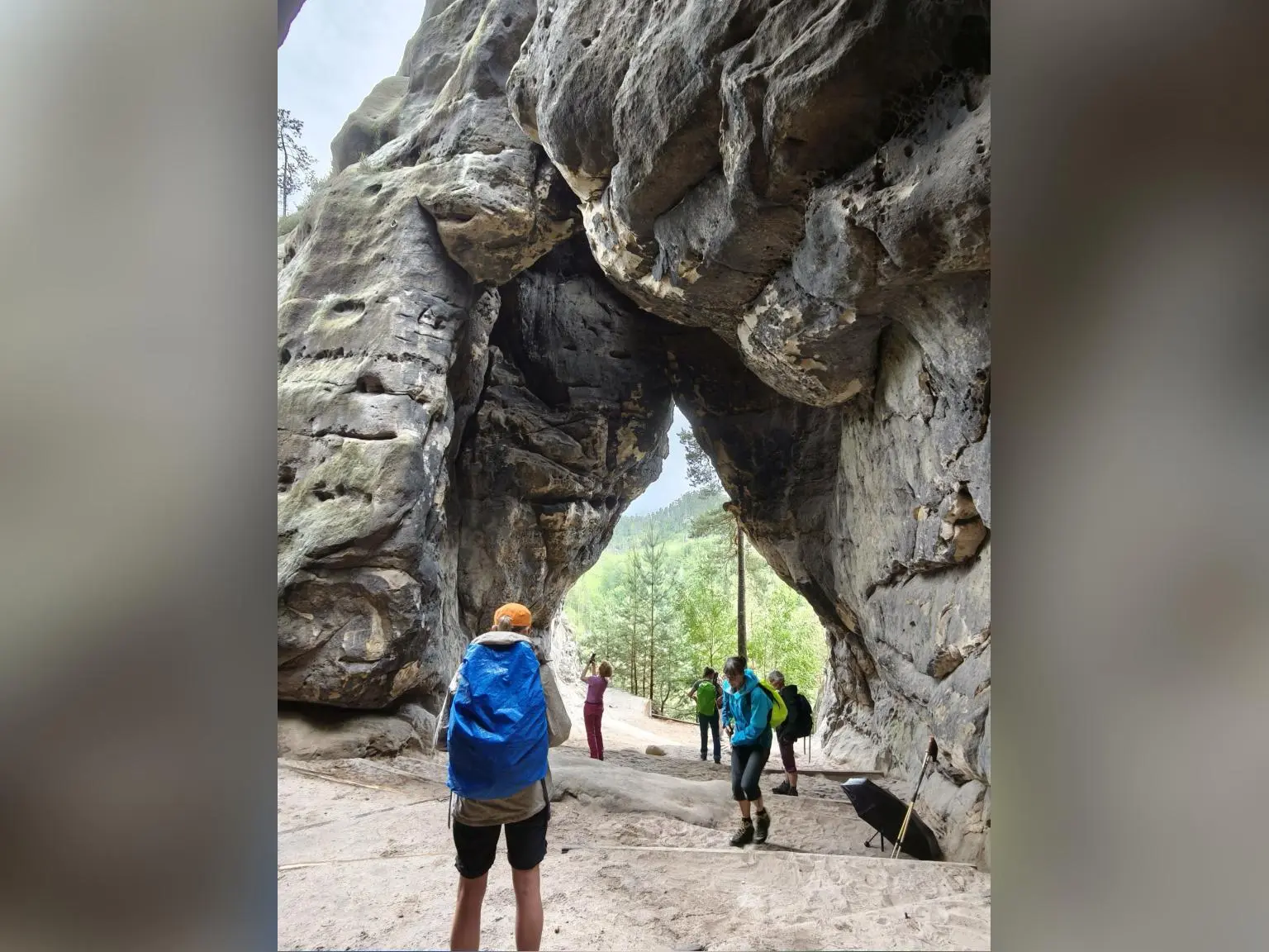 Mehrere Wandernde stehen unter einem imposanten natürlichen Felsbogen aus Sandstein. Durch die Öffnung fällt Licht auf den Weg und die bewaldete Landschaft dahinter. | © DAV Markt Schwaben/Erwin&Ursula Matzinger