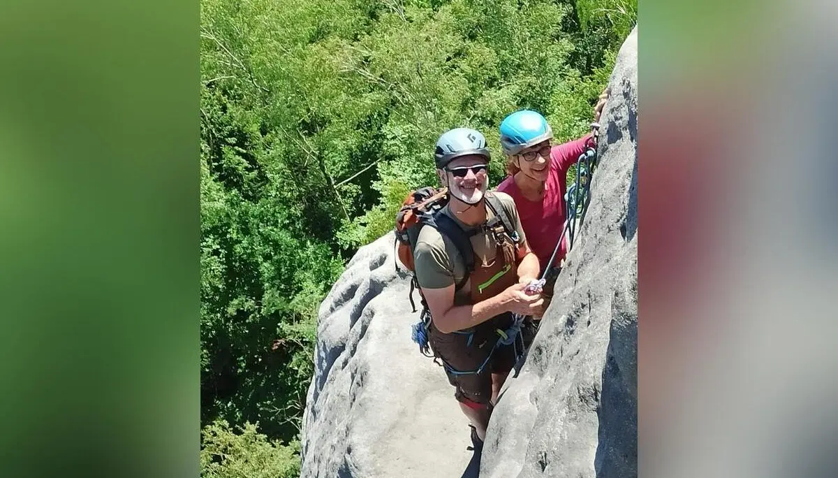 Zwei gesicherte Personen mit Kletterhelmen stehen auf einem schmalen Absatz einer steilen Sandsteinwand. Unter ihnen reicht dicht bewaldetes Gelände bis an den Felsfuß. | © DAV Markt Schwaben/Erwin&Ursula Matzinger
