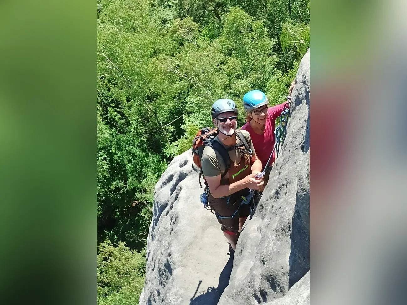 Zwei gesicherte Personen mit Kletterhelmen stehen auf einem schmalen Absatz einer steilen Sandsteinwand. Unter ihnen reicht dicht bewaldetes Gelände bis an den Felsfuß. | © DAV Markt Schwaben/Erwin&Ursula Matzinger