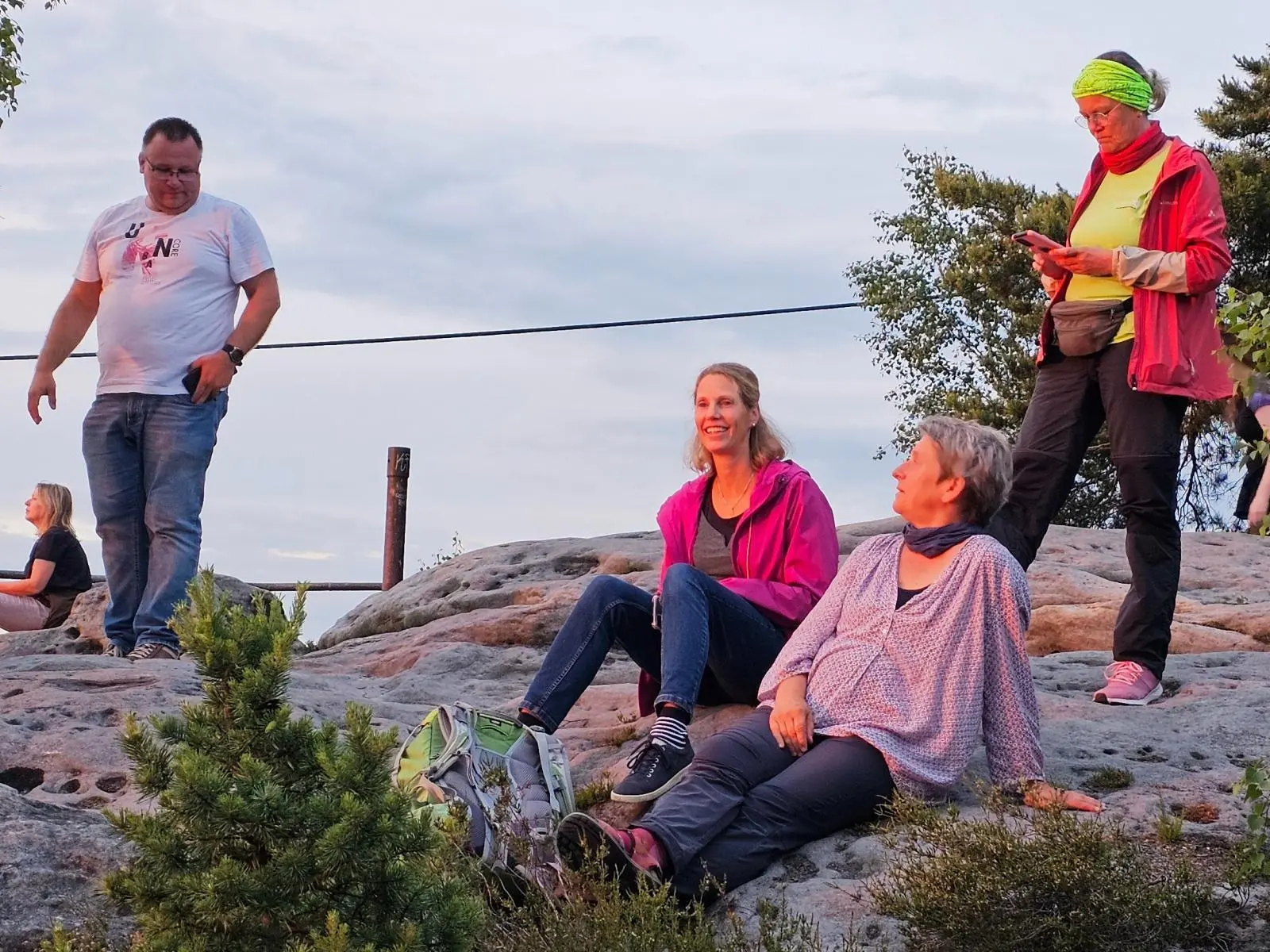 Mehrere Tourenteilnehmende sitzen und stehen auf einer Sandsteinfläche beim Sonnenuntergang. Warmes Abendlicht beleuchtet Felsen, Rucksäcke und die Aussichtskanzel. | © DAV Markt Schwaben/Lutz Gründel