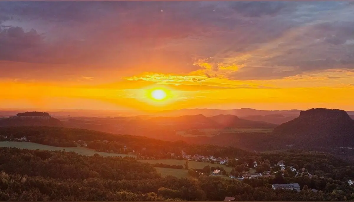 Die tief stehende Sonne taucht Felsberge, Wälder und Dörfer der Sächsischen Schweiz in warmes Abendlicht. Horizont und Wolken leuchten in Orange- und Goldtönen. | © DAV Markt Schwaben/Lutz Gründel