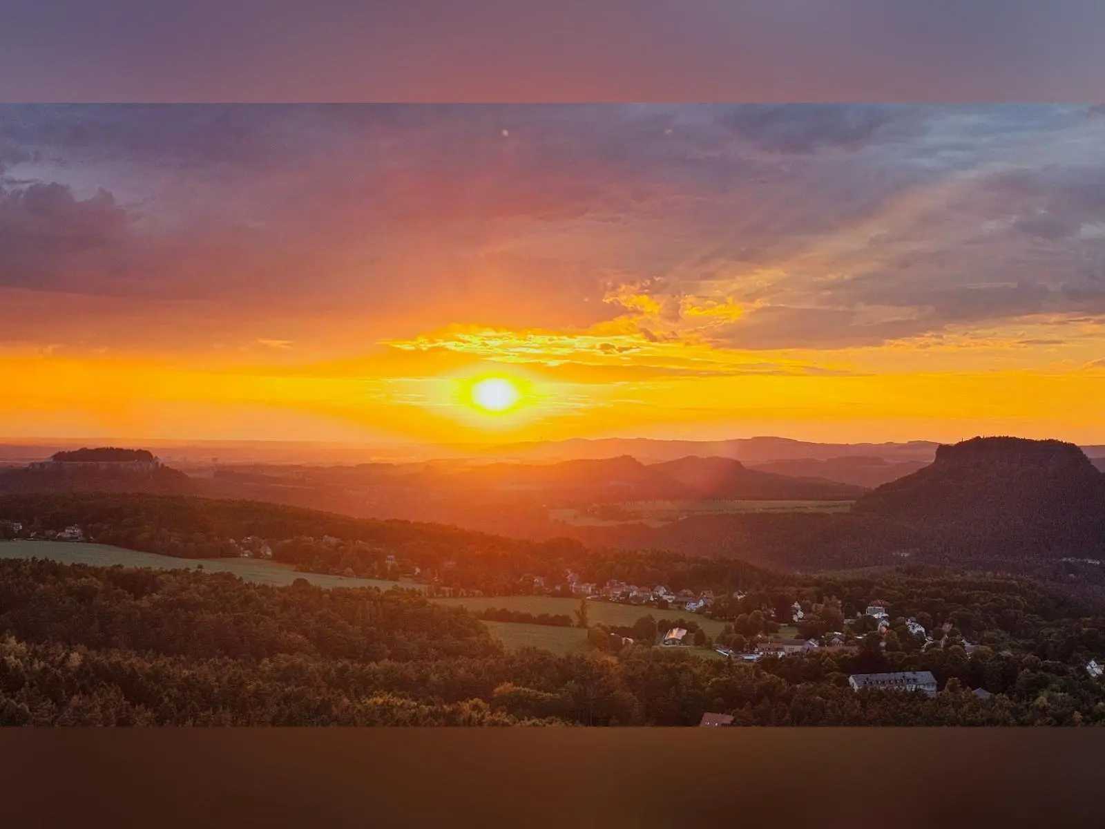 Die tief stehende Sonne taucht Felsberge, Wälder und Dörfer der Sächsischen Schweiz in warmes Abendlicht. Horizont und Wolken leuchten in Orange- und Goldtönen. | © DAV Markt Schwaben/Lutz Gründel