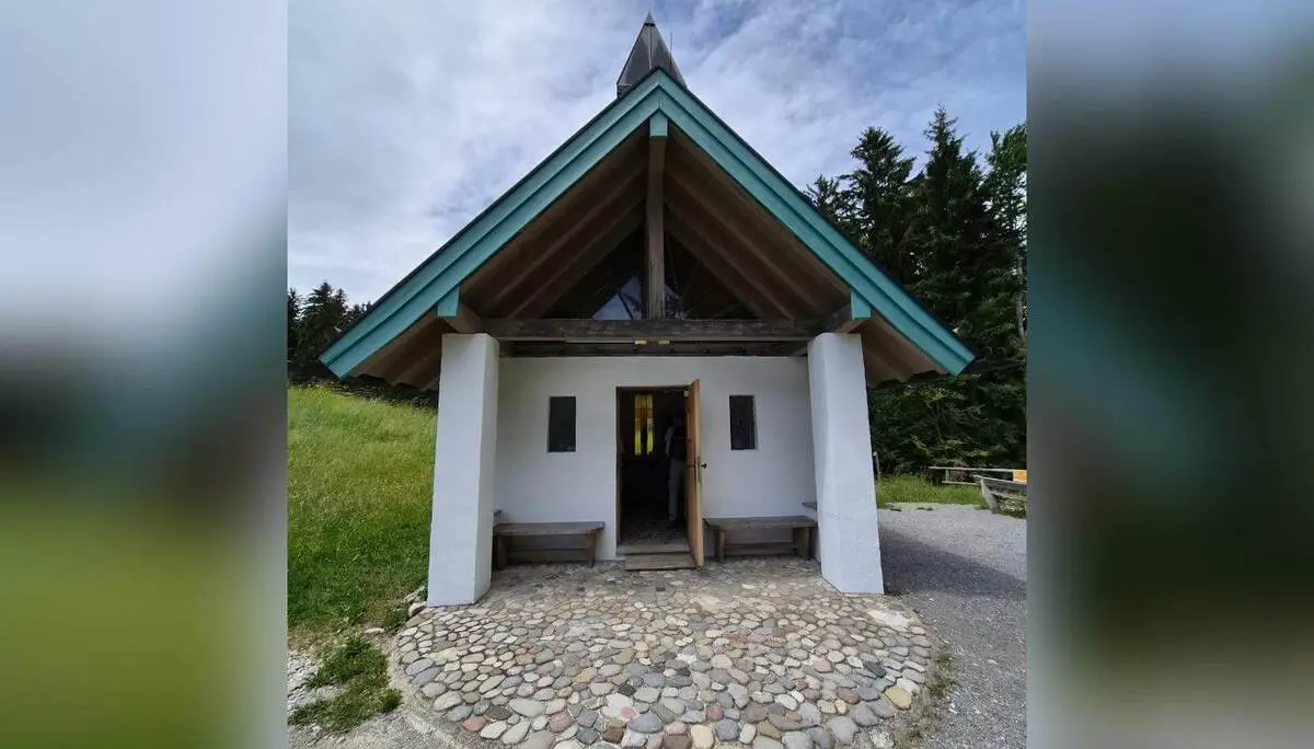 Kleine Bergkapelle mit steilem Giebeldach und offener Tür steht an einem Wegesrand, umgeben von Wiese und Wald. | © DAV Markt Schwaben / Hubert Inhofer