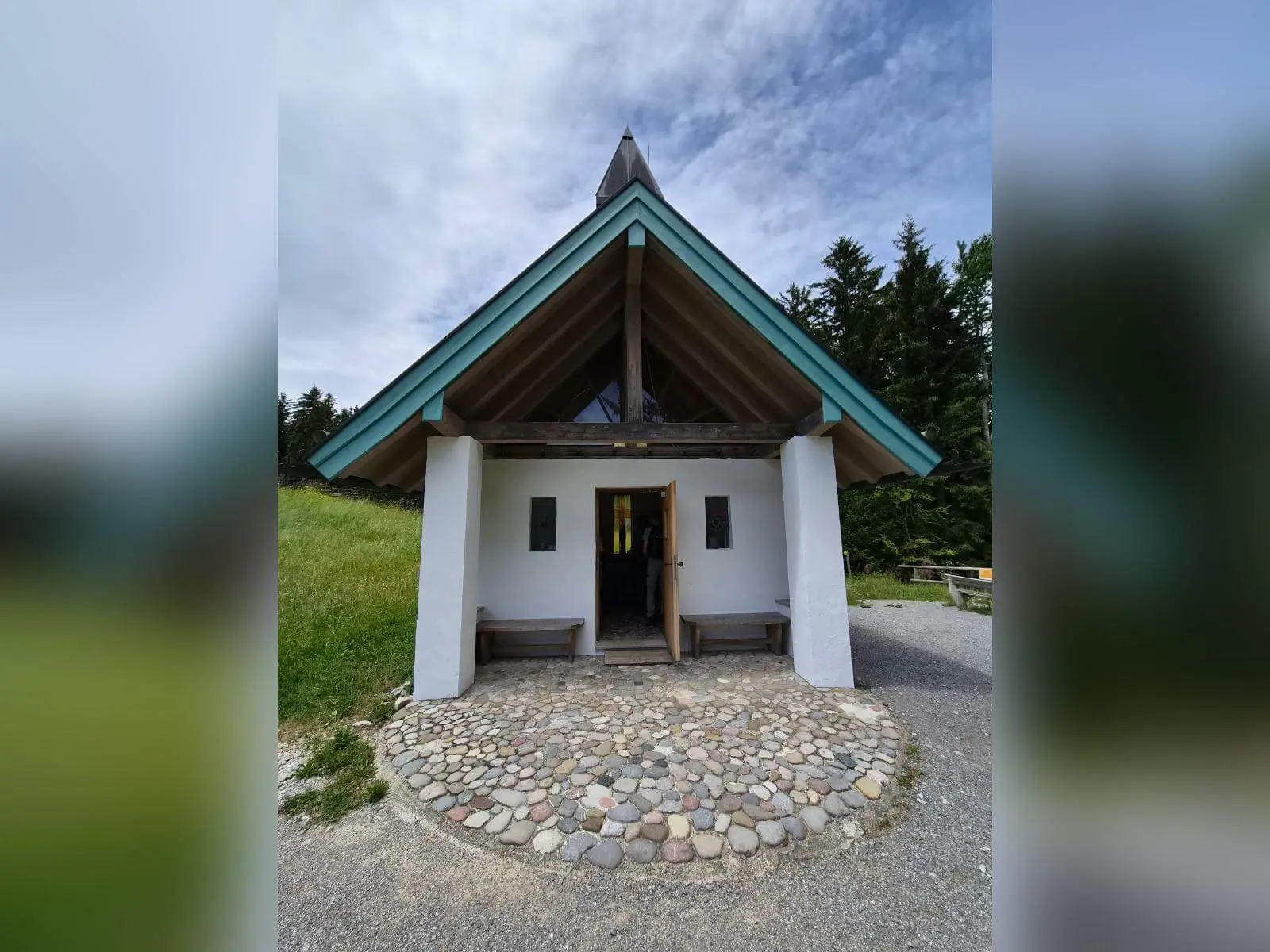 Kleine Bergkapelle mit steilem Giebeldach und offener Tür steht an einem Wegesrand, umgeben von Wiese und Wald. | © DAV Markt Schwaben / Hubert Inhofer