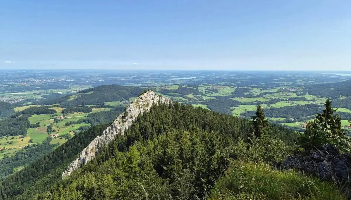 Aussicht von einer Bergwiese auf einen bewaldeten Felsrücken und das weite Alpenvorland. Felder, Wälder und Ortschaften prägen die Landschaft. | © DAV Markt Schwaben / Hubert Inhofer